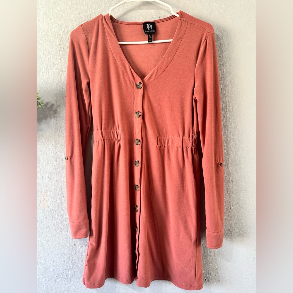 Long shirt, a peach color, with buttons on the sleeve, and buttons on the top.